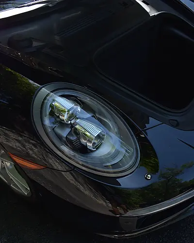 Gleaming black Porsche headlight, with the front trunk open during the detail